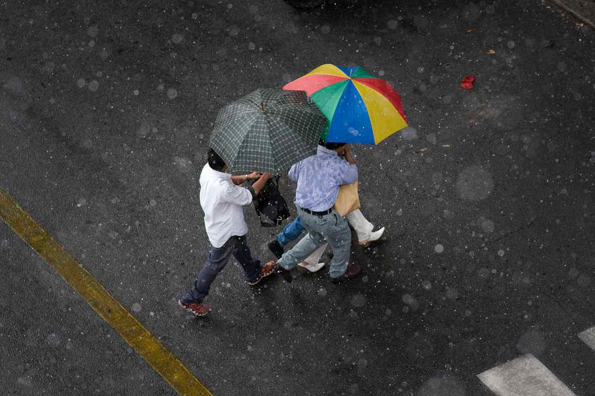 Uomini si riparano dalla pioggia in strada aprendo l'ombrello