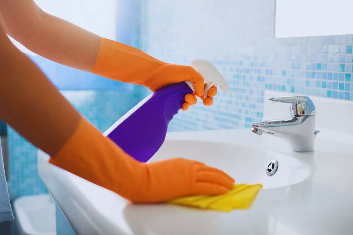 mani con guanti lavano un lavandino del bagno