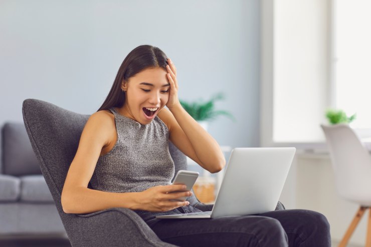 donna stupita di fronte a cellulare e pc