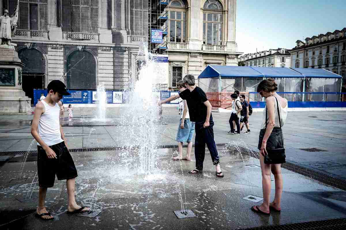 persone si rinfrescano con l'acqua di una fontana