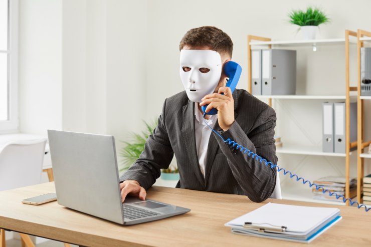 uomo al telefono con maschera bianca di fronte a pc