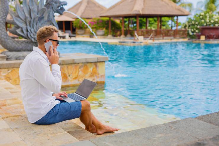 uomo seduto a bordo piscina al pc e cellulare